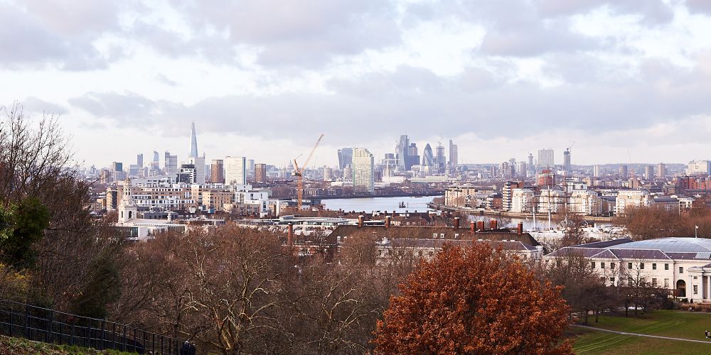 A view across London on a wintery day. Parkland can be seen in the foreground and in the distance, the City, the Shard and Canary Wharf are all visible.