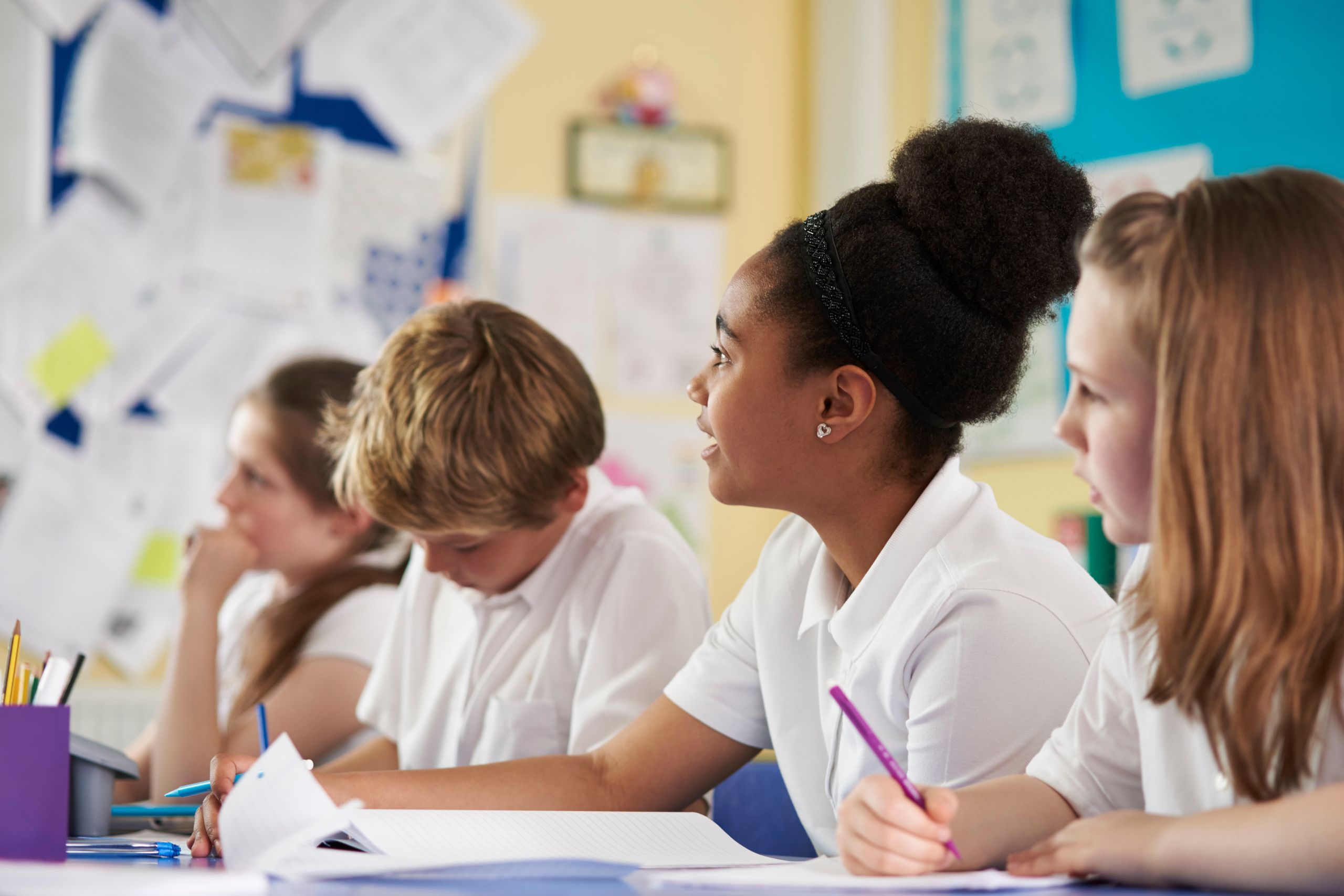 A group of school children in class listening to the teacher and taking notes