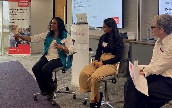 Panellists sharing their experiences at the Women's Fund for London event with CEO Kate Markey - behind them is a large screen, a podium with a laptop on it and a London Community Foundation pull-up banner.