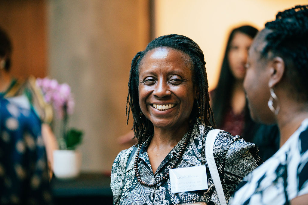 Two people chatting together at the VAWG Grassroots Fund celebration event, with other people visible in the background but out of focus.